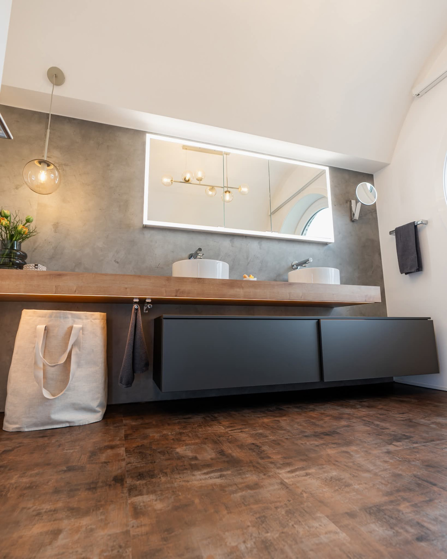 Modernes Bad mit fugenloser Betonoptik-Wand, schwebendem Holzwaschtisch und beleuchtetem Spiegelschrank
